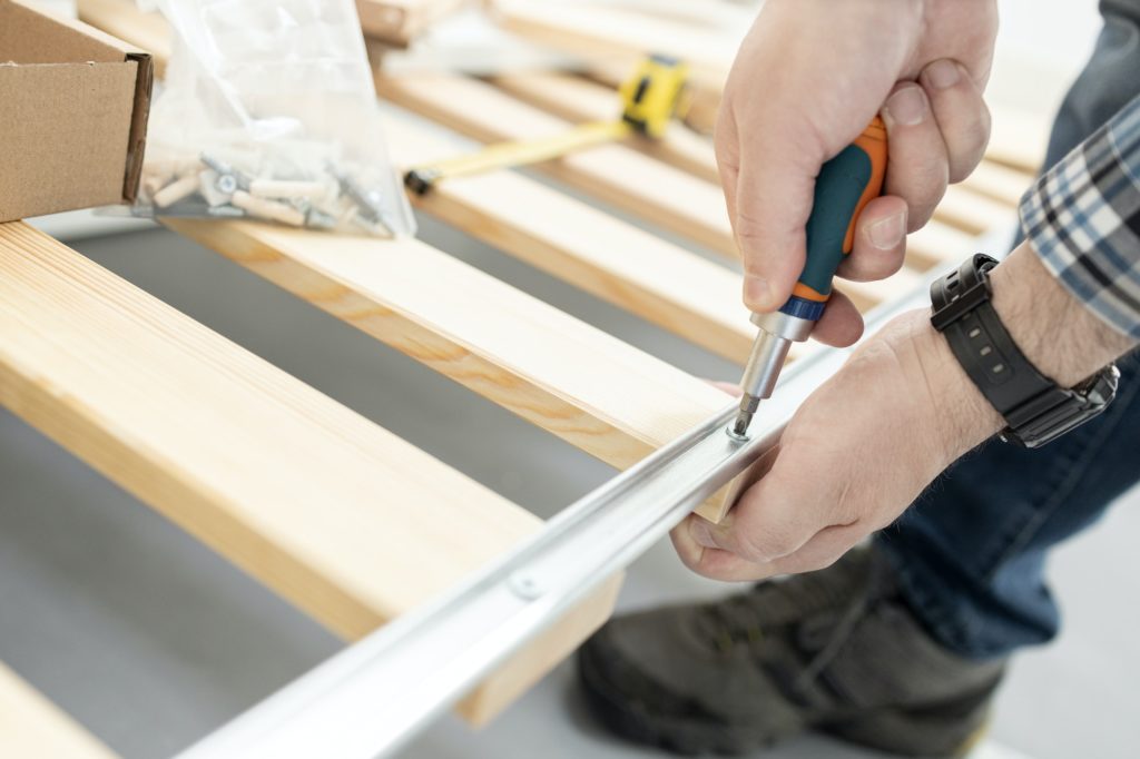 Close up of hands assembling a split box spring with a screwdriver.