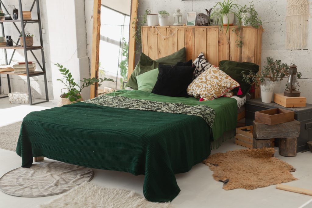 Comfortable bed with new green linens in eco style room interior