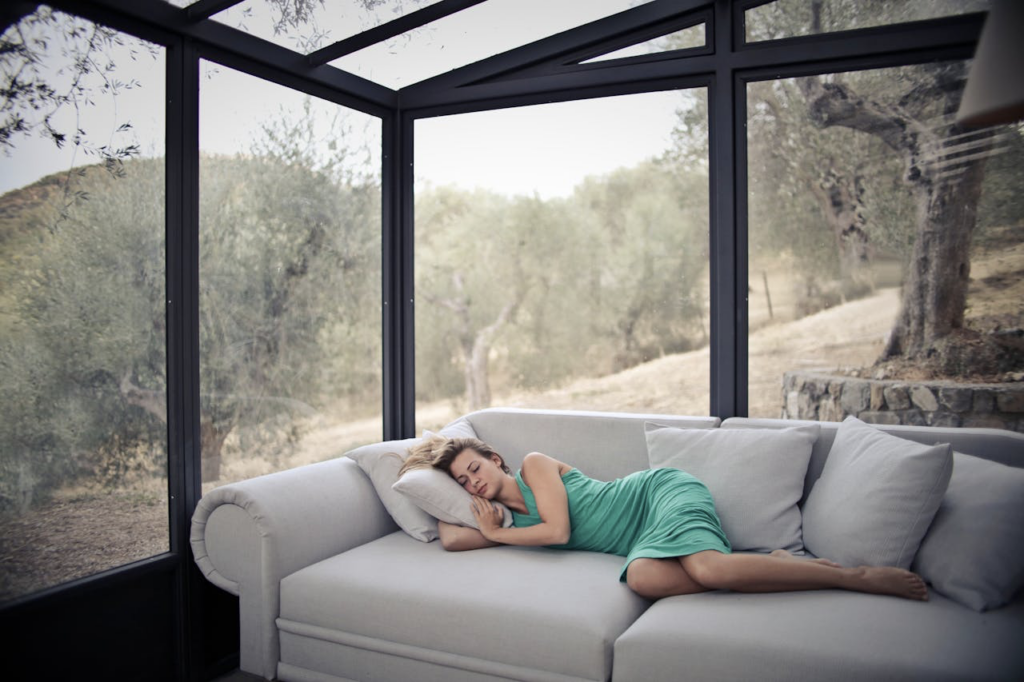 A woman sleeping on a couch next to large windows